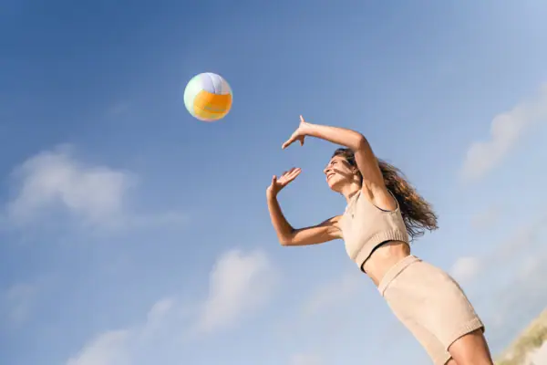 Beachvolleyball St. Peter-Ording Eine Frau wirft eine. Beachvolleyball nach oben über ihrem Kopf und der blaue Himmel ist im Hintergrund zu sehen.