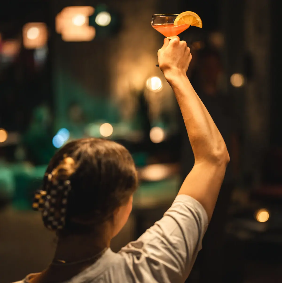 Drink Drifters Hang Out Eine Frau hält ein Glas mit einem Drink hoch.