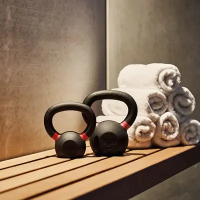 Fitnessbereich im Alpine Swim Club Zwei Kettlebells und mehrere aufgerollte Handtücher auf einer Holzbank in einem modernen Fitness- oder Wellnessbereich