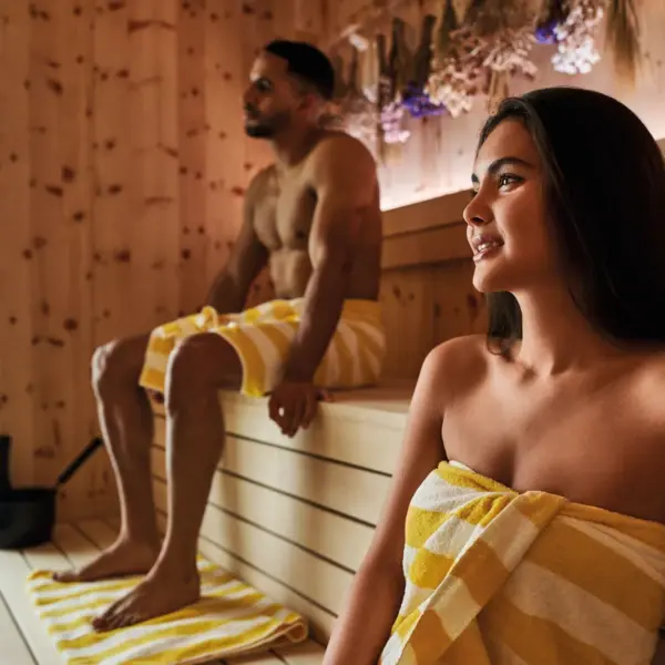 Bio-Sauna im Alpine Swim Club Mann und Frau beim Saunieren in moderner Holzsauna mit Kräutern mit gelb-weiß gestreiften Handtüchern