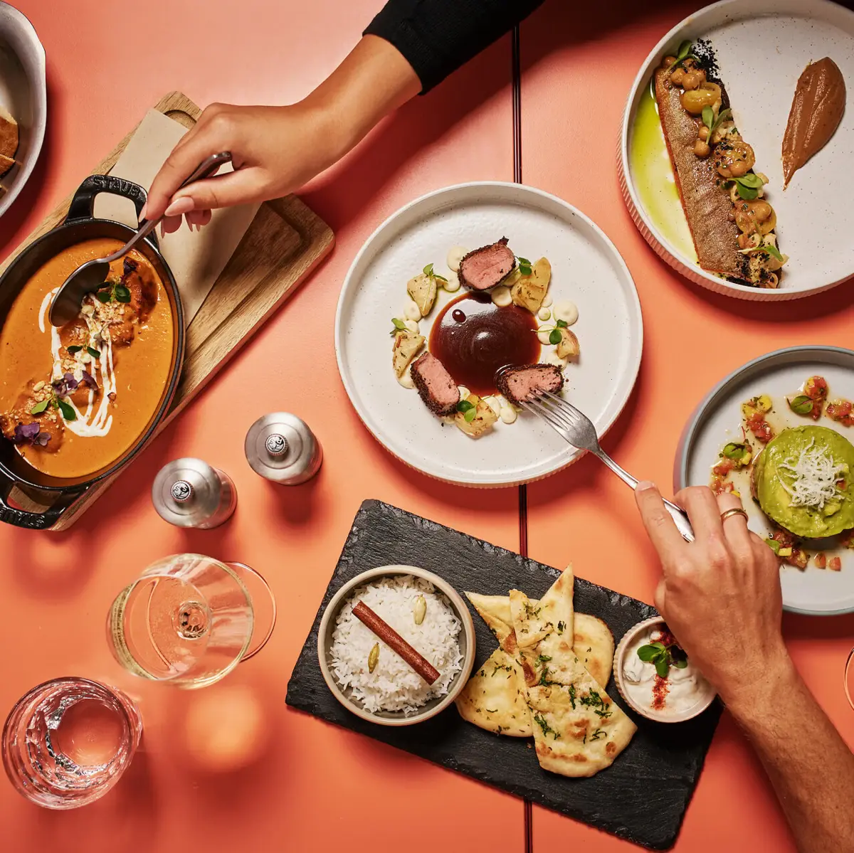 Kulinarische Vielfalt in Auntie Heidis Restaurant Bunte Auswahl an regionalen und mediterranen Spezialitäten auf einer orangenen Tischplatte mit Fleisch, Getränken und Vorspeisen