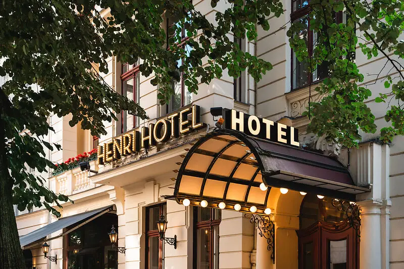 HENRI Hotel in Berlin Eingang des HENRI Hotels in Berlin mit klassischem, eleganten Schriftzug und begrüntem Vordach, umgeben von alten Bäumen und historischer Fassade