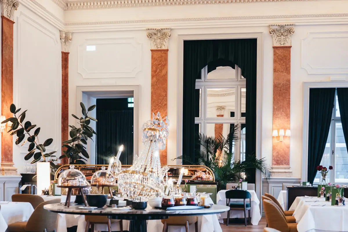 Straubinger Speisesaal Ein historischer Speisesaal mit Tischen und Stühlen und einem Kronleuchter.