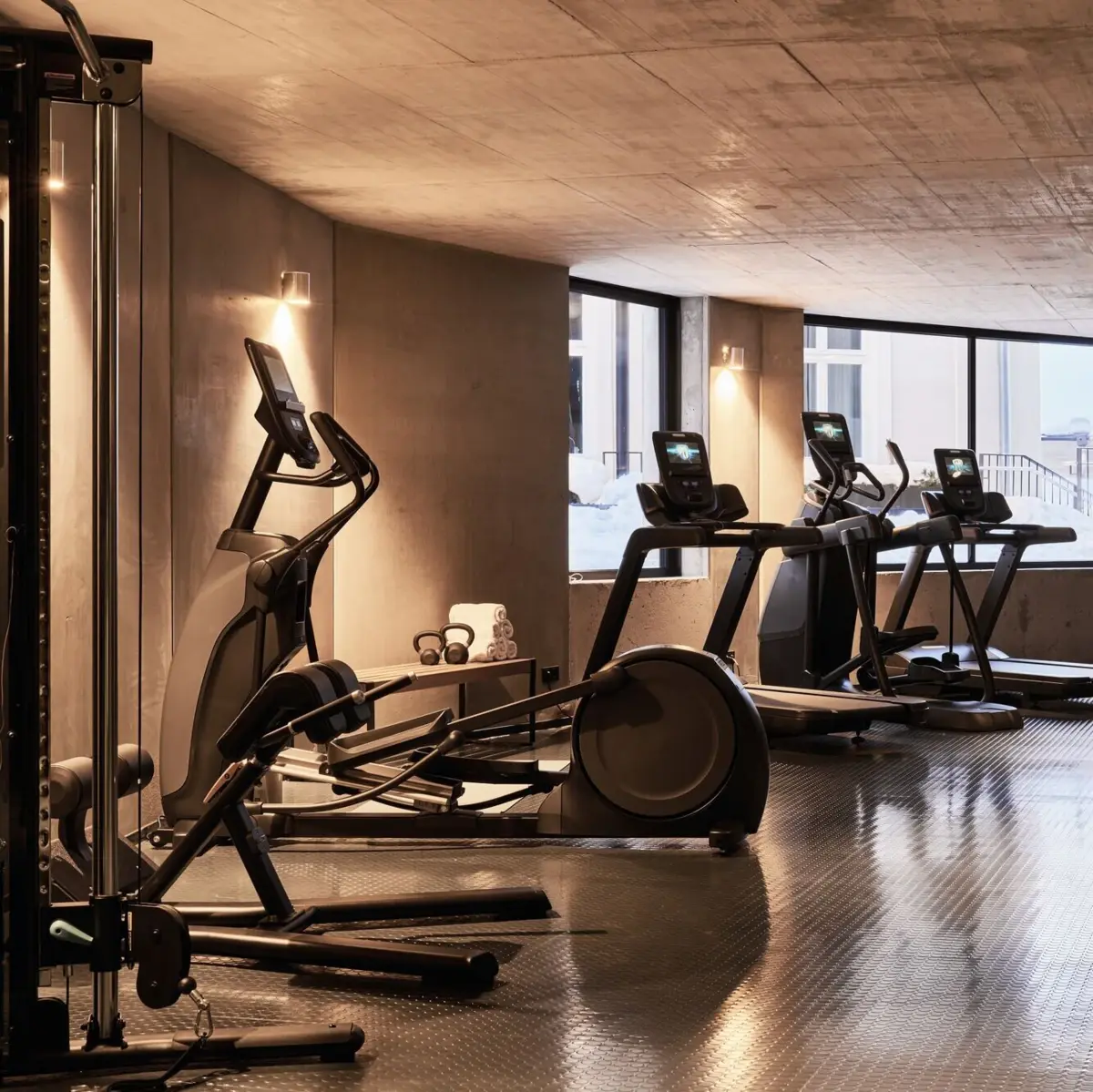 Fitnessraum im Urban Nature Bad Gastein Moderner Fitnessraum mit Crosstrainer, Laufbändern und Kraftstation in elegantem Beton-Design und Tageslicht