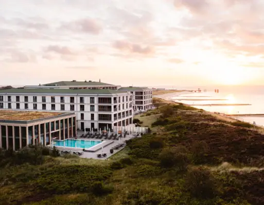 A-ROSA Hotel auf Sylt Modernes Hotel mit Außenpool direkt an der Küste, umgeben von Dünenlandschaft, Sonnenaufgang über der Nordsee im Hintergrund