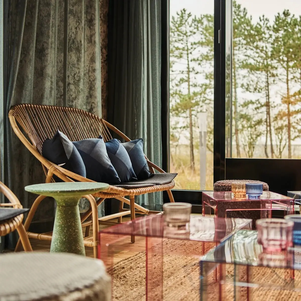 Sitzecke Drifters Hang Out Eine Sitzecke mit mehreren Sitzmöglichkeiten, Hockern und kleinen Tischen vor einem großem Fenster mit Blick ins Grüne.