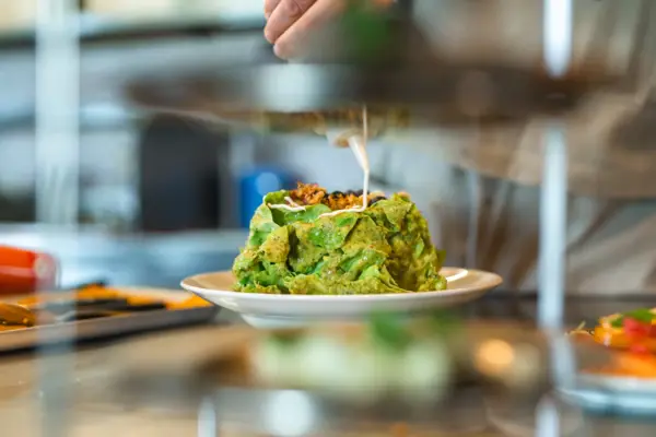 Gericht Auntie Clara Restaurant Ein Koch richtet ein grünes Tellergericht auf einer Küchenarbeitsplatte an.