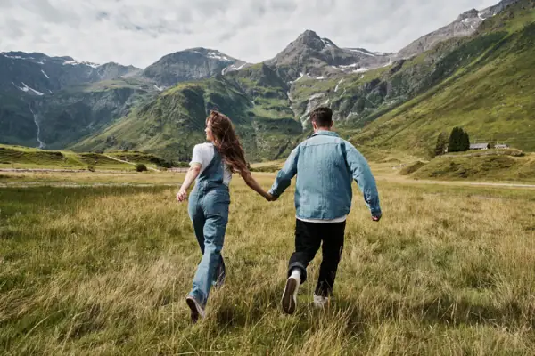 Sommer Bad Gastein Ein Mann und eine Frau halten sich an den Händen in einem Feld mit Bergen im Hintergrund.