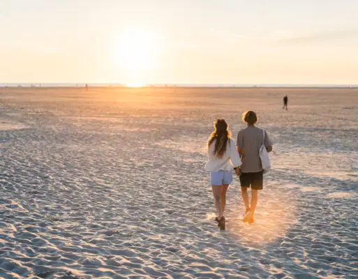 Strand St. Peter-Ording Ein Pärchen läuft Hand in Hand an einem Strand bei Sonnenuntergang lang.