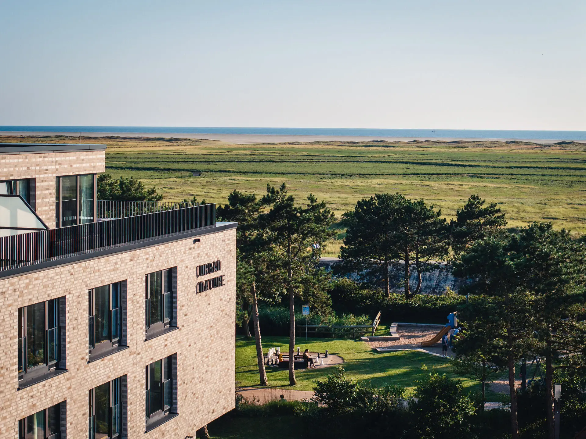 Urban Nature St. Peter-Ording Ein Gebäude mit einem Spielplatz und einem Grasfeld.