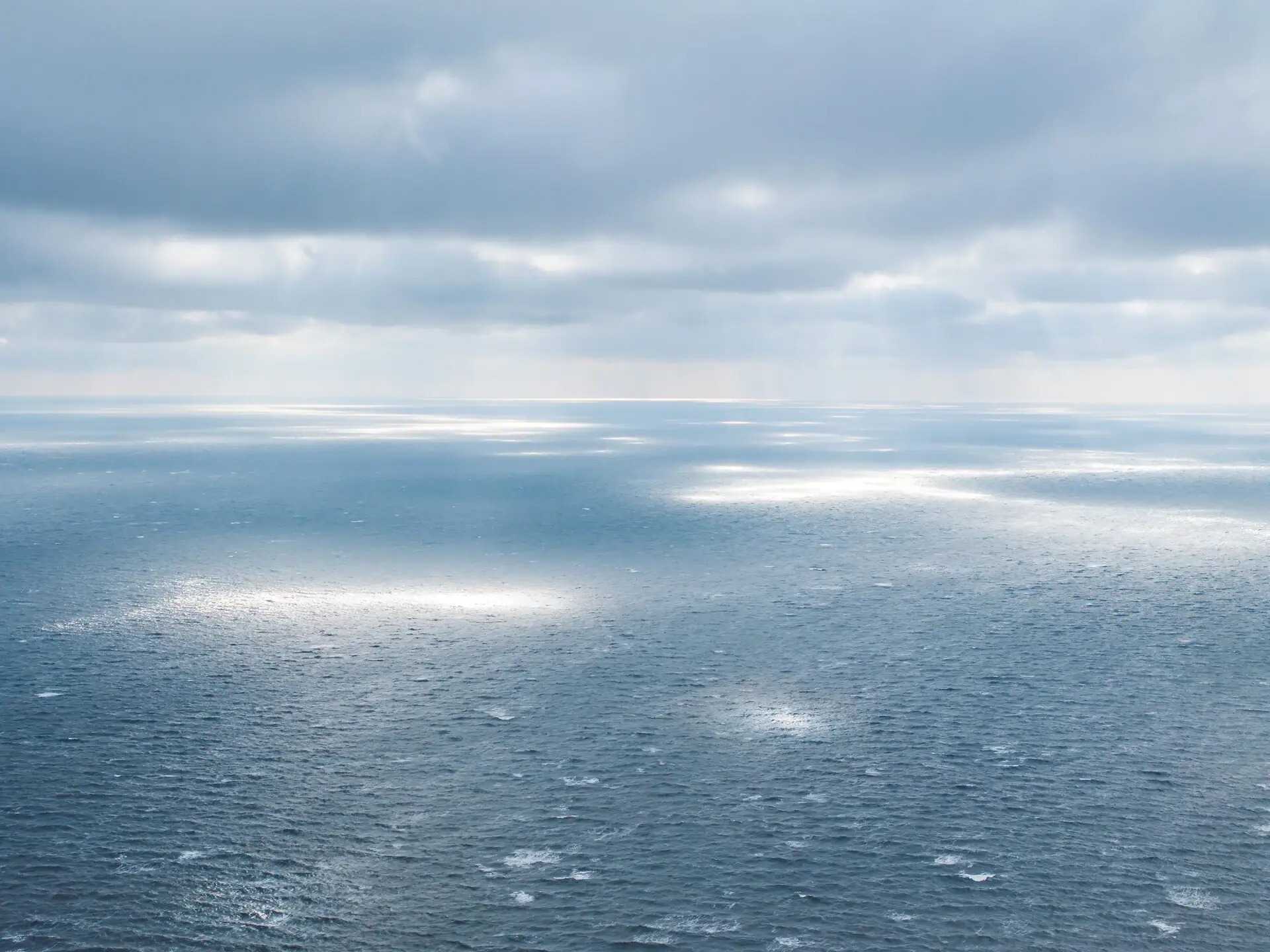 Meer Winter Großer Wasserkörper mit Sonnenstrahlen, die durch die Wolken scheinen.